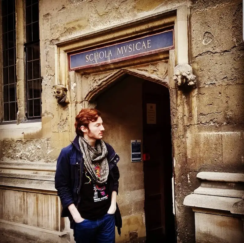 Student standing beside the entrance of a historic university music school building