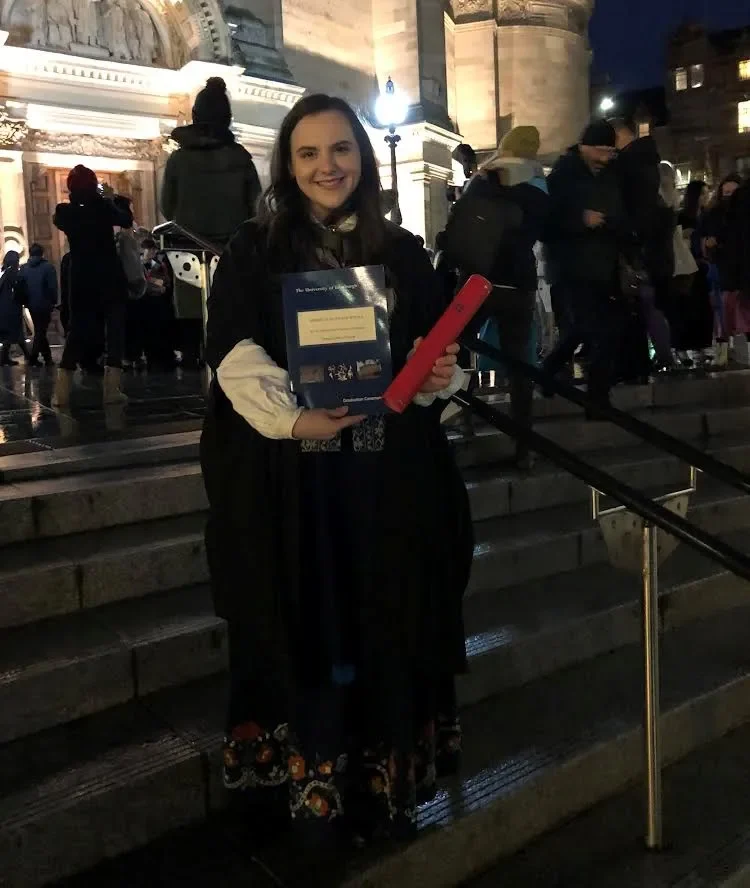 Graduate student holding a diploma during an outdoor evening ceremony.