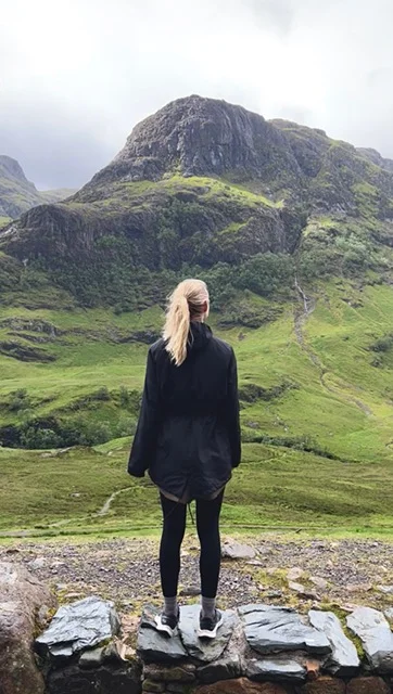 Person standing on rocks facing a green mountain landscape.
