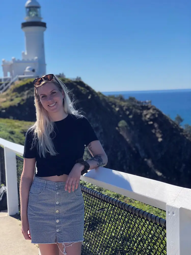 Student standing by a railing with a lighthouse and ocean in the background.