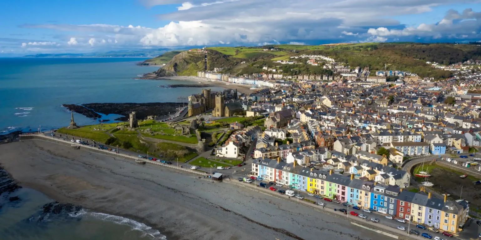 Luftbilde av Aberystwyth med slottsruiner, fargerike hus og kysten i Wales.