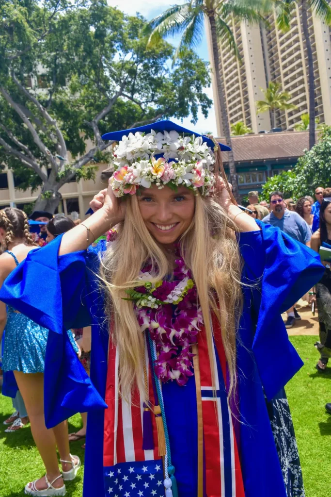 Student i blå kappe med blomsterkranser feirer graduering ved universitet på Hawaii