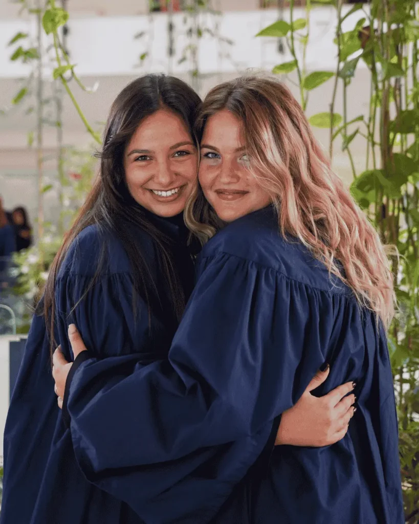 To studenter feirer uteksamineringen ved European University of Rome iført akademiske kapper og smiler sammen.