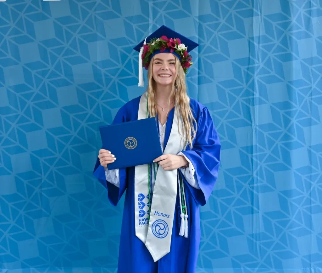 Student i kappe og lue holder vitnemålet foran Hawaii Pacific University i Honolulu på Hawaii.
